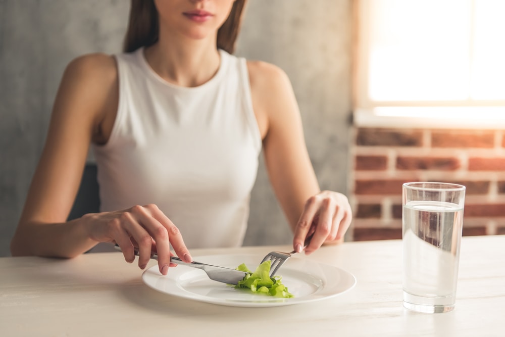 Thin Woman with a Small Amount of Food on a Plate and a Glass of Water to Demonstrate Eating Disorders